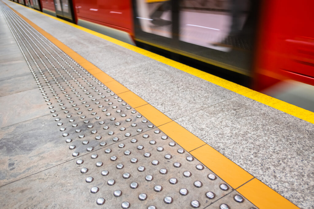 blurred red subway train, diagonal tactile paving also called detectable warning surfaces for visually impared. yellow line