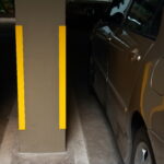 Closeup corner guard or column protector in parking lot with two cars parked. This corner guard is attached to concrete column. It can reduce damages caused by car impact